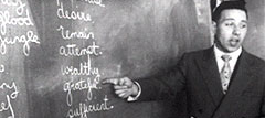 A black and white photograph of a residential school instructor pointing to English words on a blackboard.